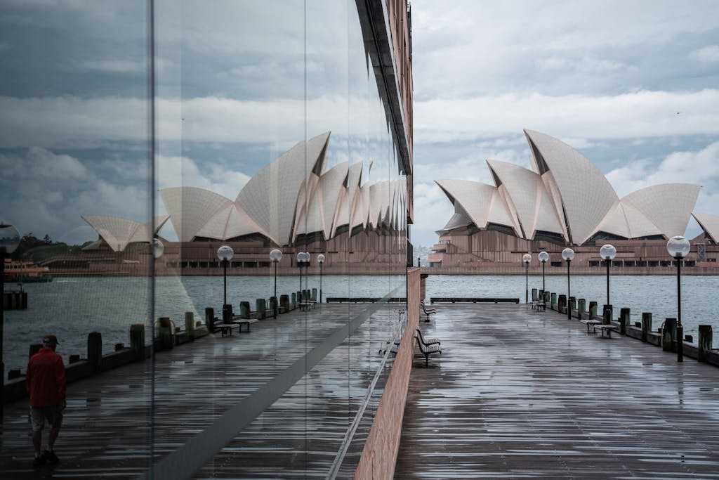Exterior of modern white Sydney Opera House with unusual futuristic design located on city harbor and reflecting in neighbor building glass wall in daylight